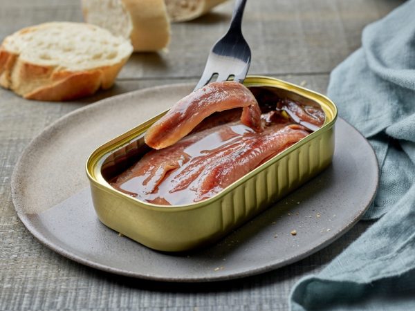 canned anchovy fillets and slices of baguette on wooden kitchen table