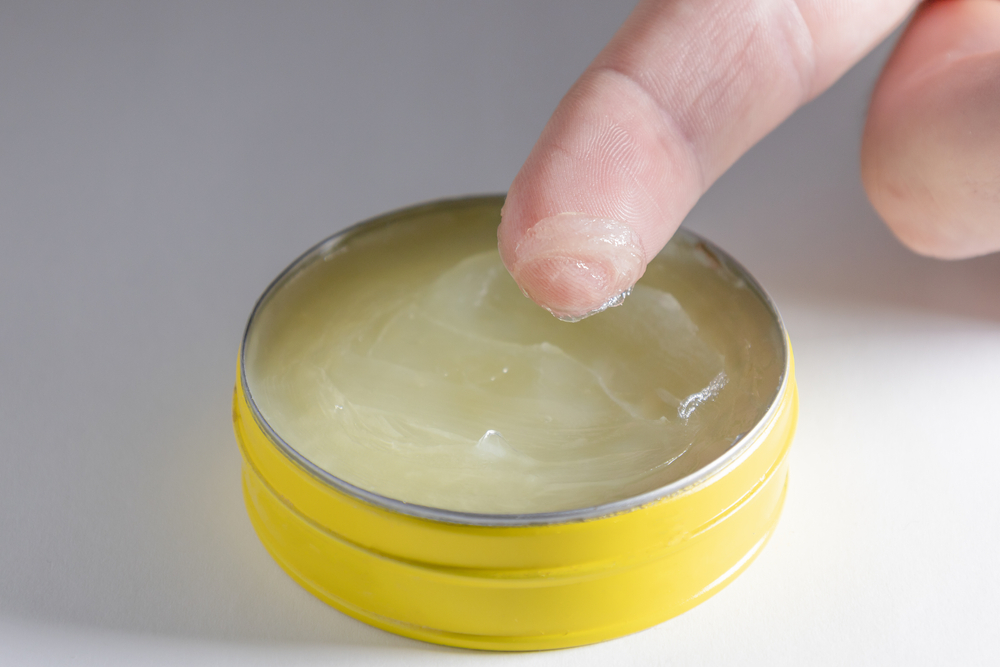 Finger in small yellow jar of vaseline