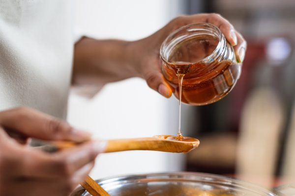 woman pouring honey to wooden spoon