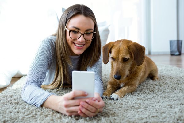 young woman using phone with her dog at home